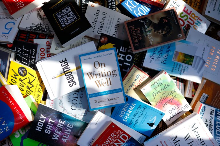 Tumpukan berbagai buku pengembangan diri, psikologi, dan keuangan yang tersebar di atas permukaan.