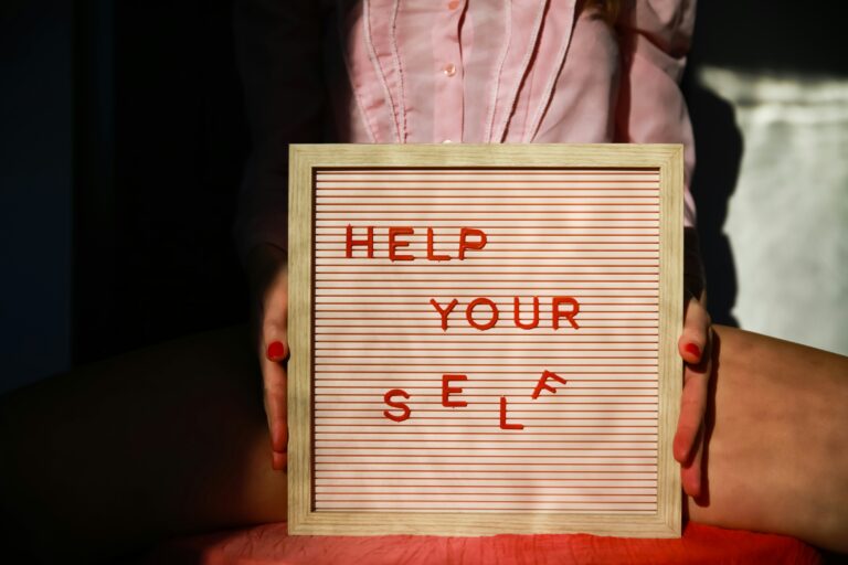 Seseorang memegang papan dengan tulisan "HELP YOUR SELF" yang sebagian hurufnya terjatuh.